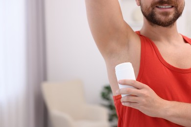 Smiling man applying solid deodorant at home, closeup. Space for text