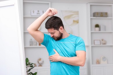 Photo of Emotional man in t-shirt before using deodorant at home