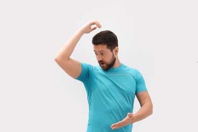 Emotional man in t-shirt before using deodorant on white background