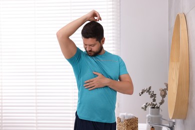 Emotional man in t-shirt before using deodorant at home