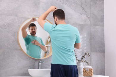 Photo of Emotional man in t-shirt before using deodorant near mirror at home, back view