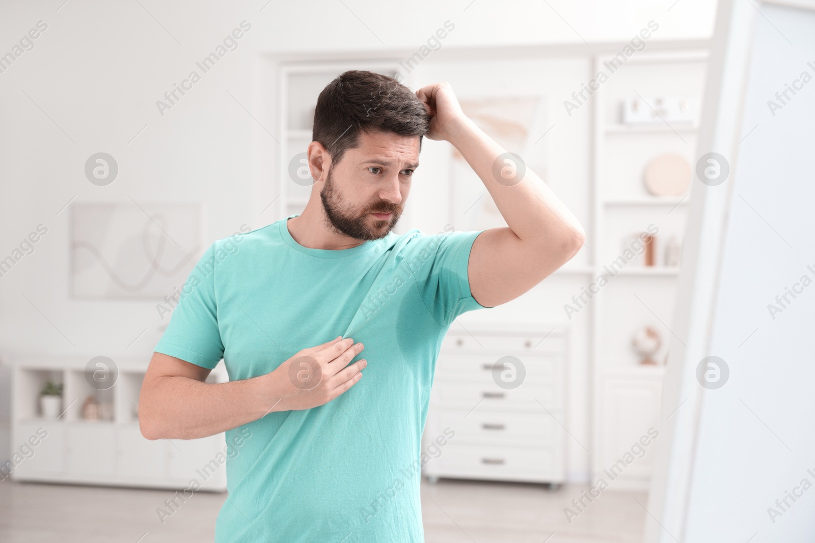 Photo of Emotional man in t-shirt before using deodorant at home