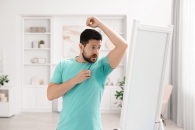 Photo of Emotional man in t-shirt before using deodorant at home