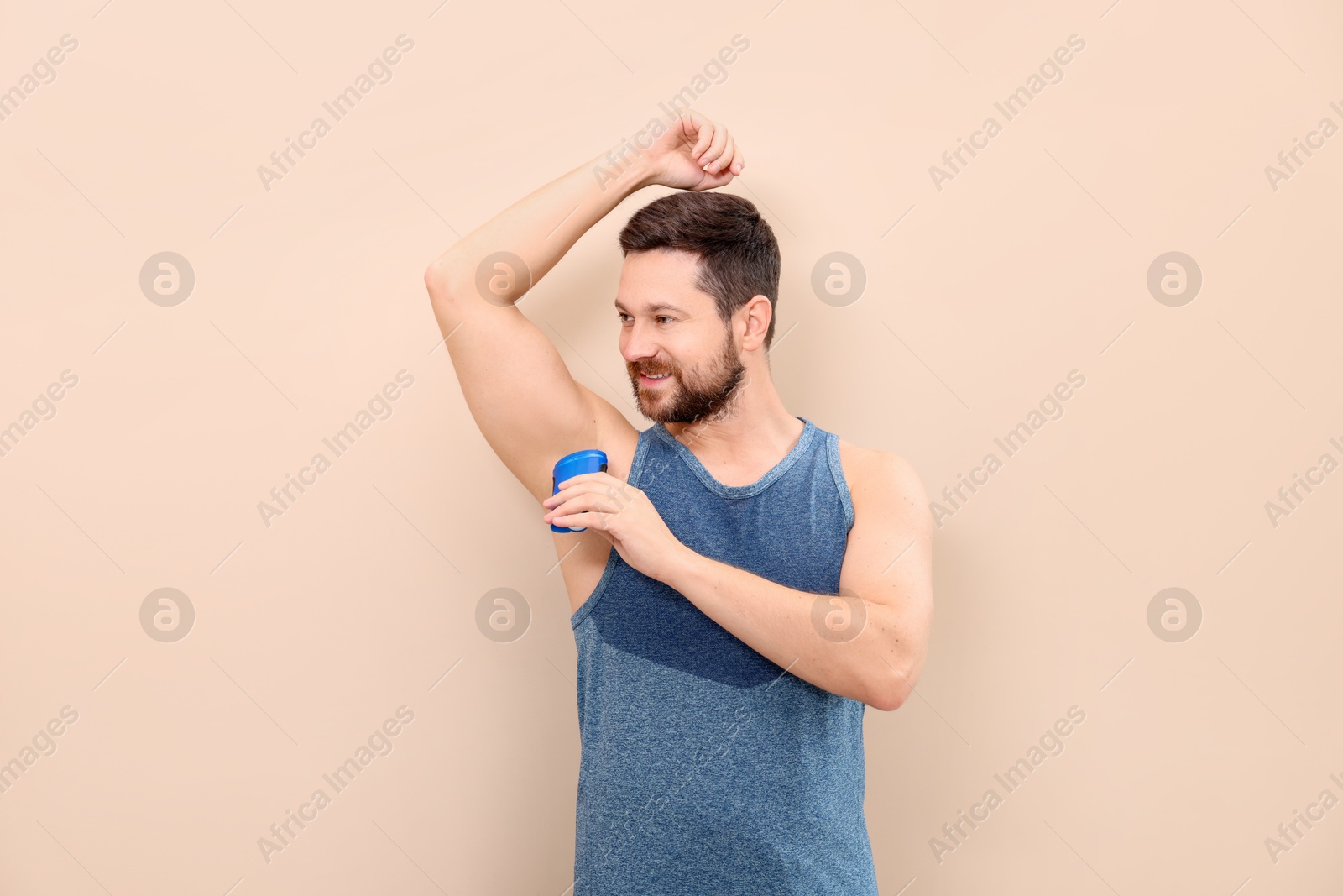 Photo of Smiling man applying solid deodorant on beige background