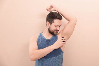 Photo of Man applying roll-on deodorant on beige background