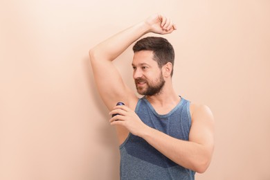 Smiling man applying roll-on deodorant on beige background. Space for text