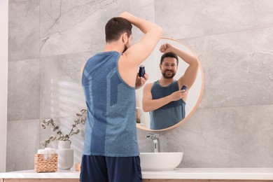 Smiling man applying roll-on deodorant near mirror at home, back view