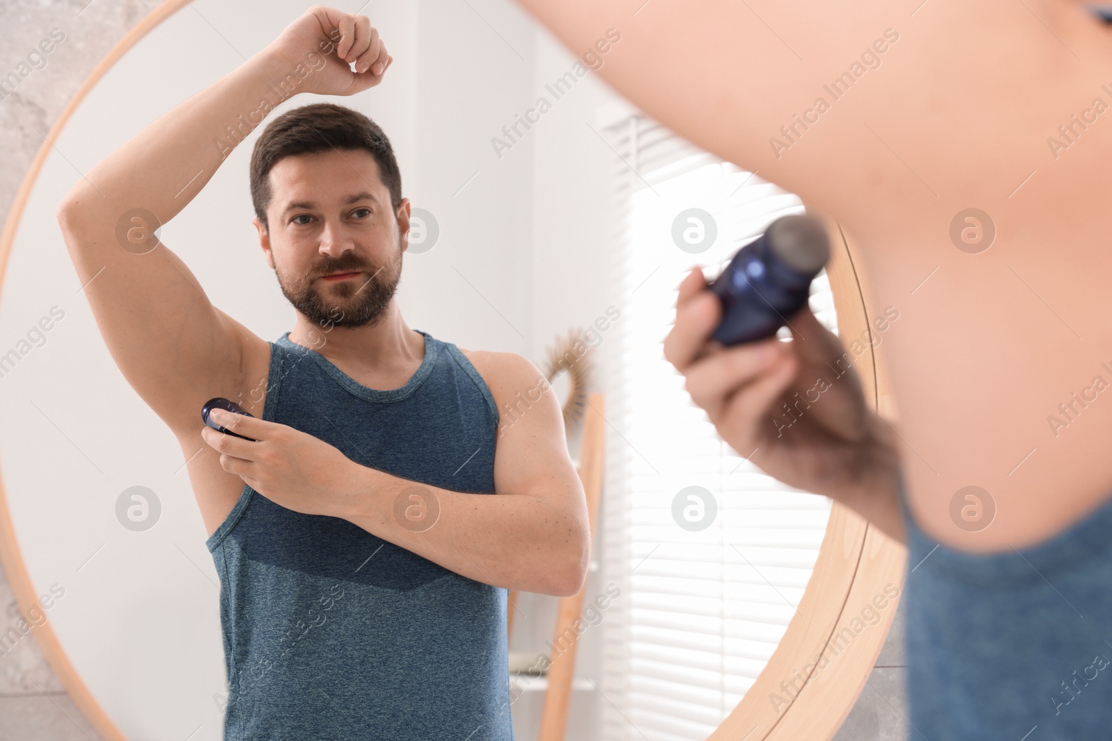 Photo of Man applying roll-on deodorant near mirror at home