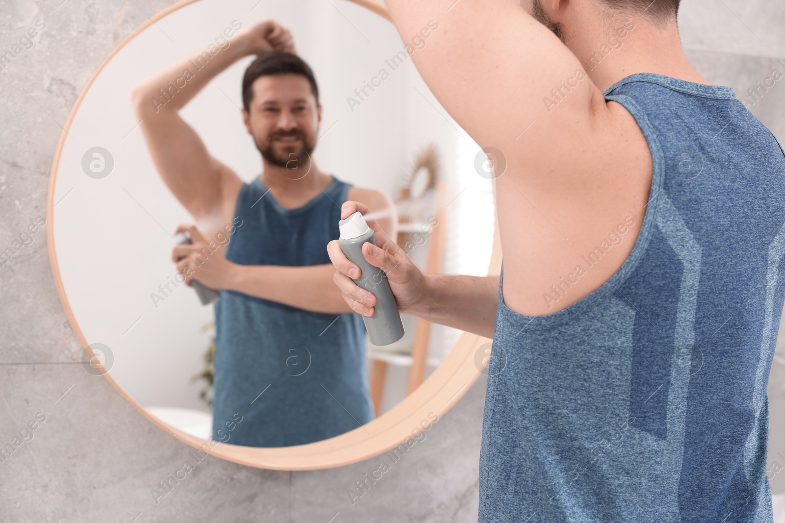 Photo of Man applying spray deodorant near mirror at home, selective focus