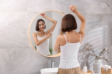 Smiling woman applying roll-on deodorant near mirror at home, back view