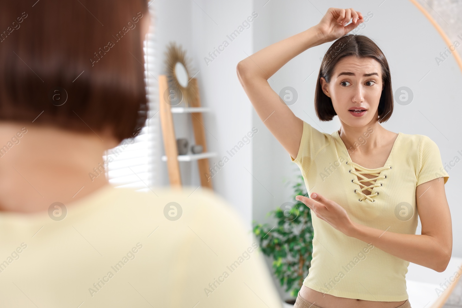 Photo of Emotional woman in t-shirt before using deodorant near mirror at home