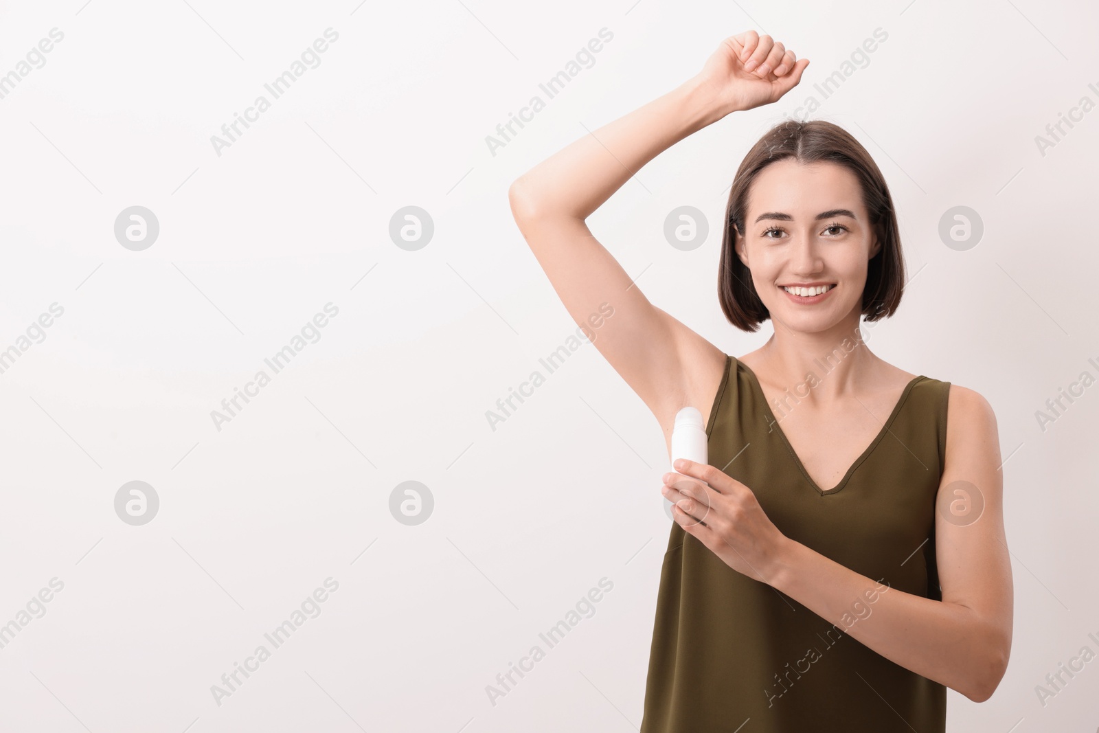 Photo of Smiling woman applying roll-on deodorant on white background. Space for text