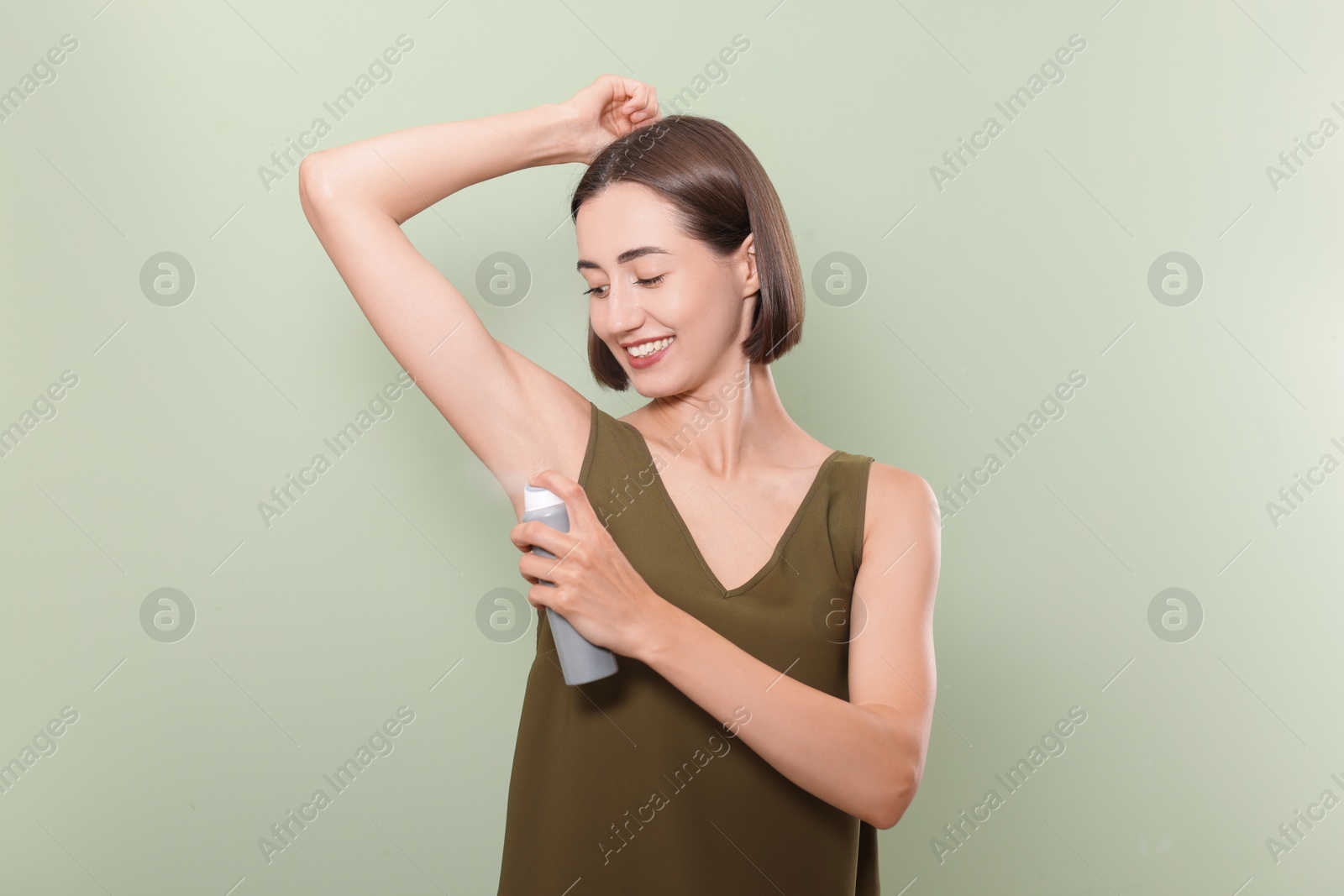 Photo of Smiling woman applying spray deodorant on green background