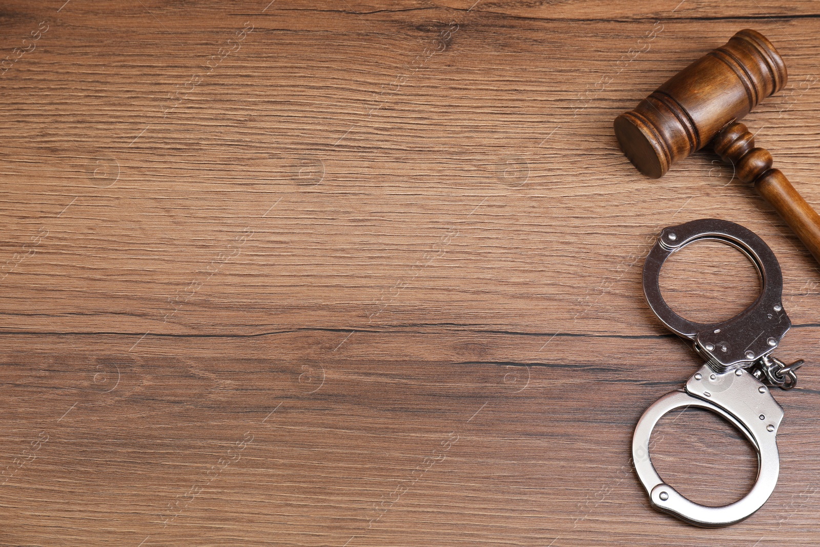 Photo of Judge's gavel and handcuffs on wooden table, flat lay. Space for text