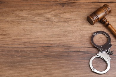 Judge's gavel and handcuffs on wooden table, flat lay. Space for text