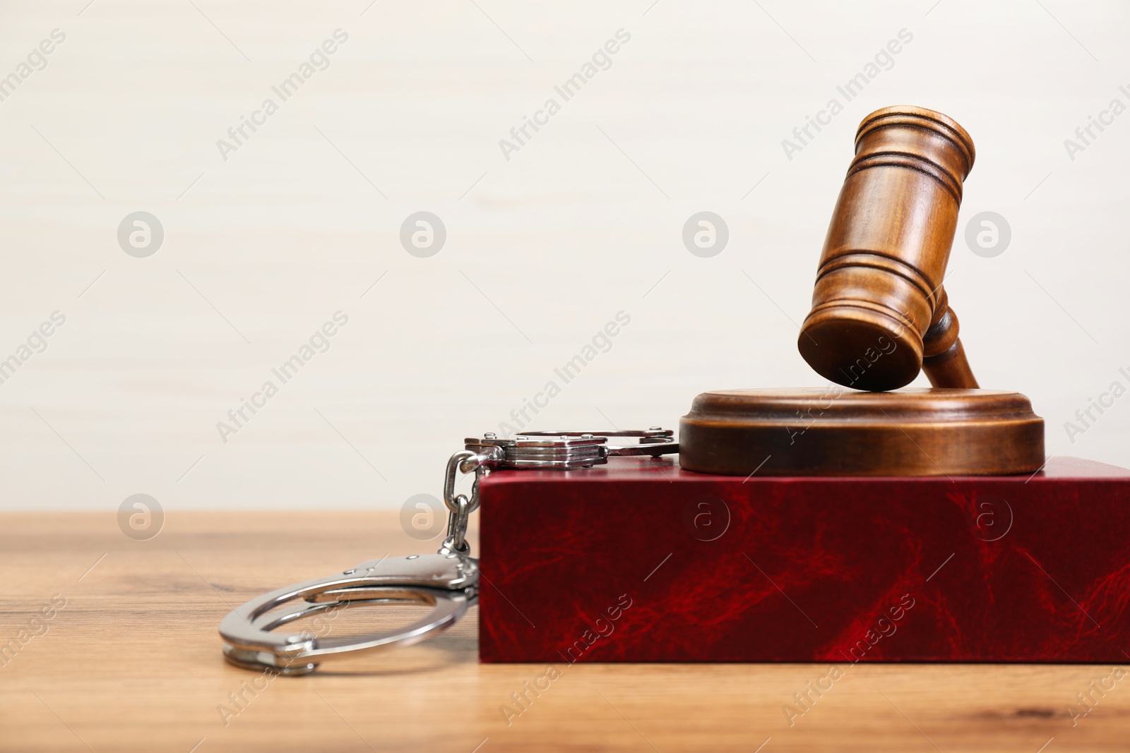 Photo of Book, judge's gavel and handcuffs on wooden table, space for text