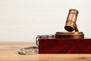 Photo of Book, judge's gavel and handcuffs on wooden table, space for text