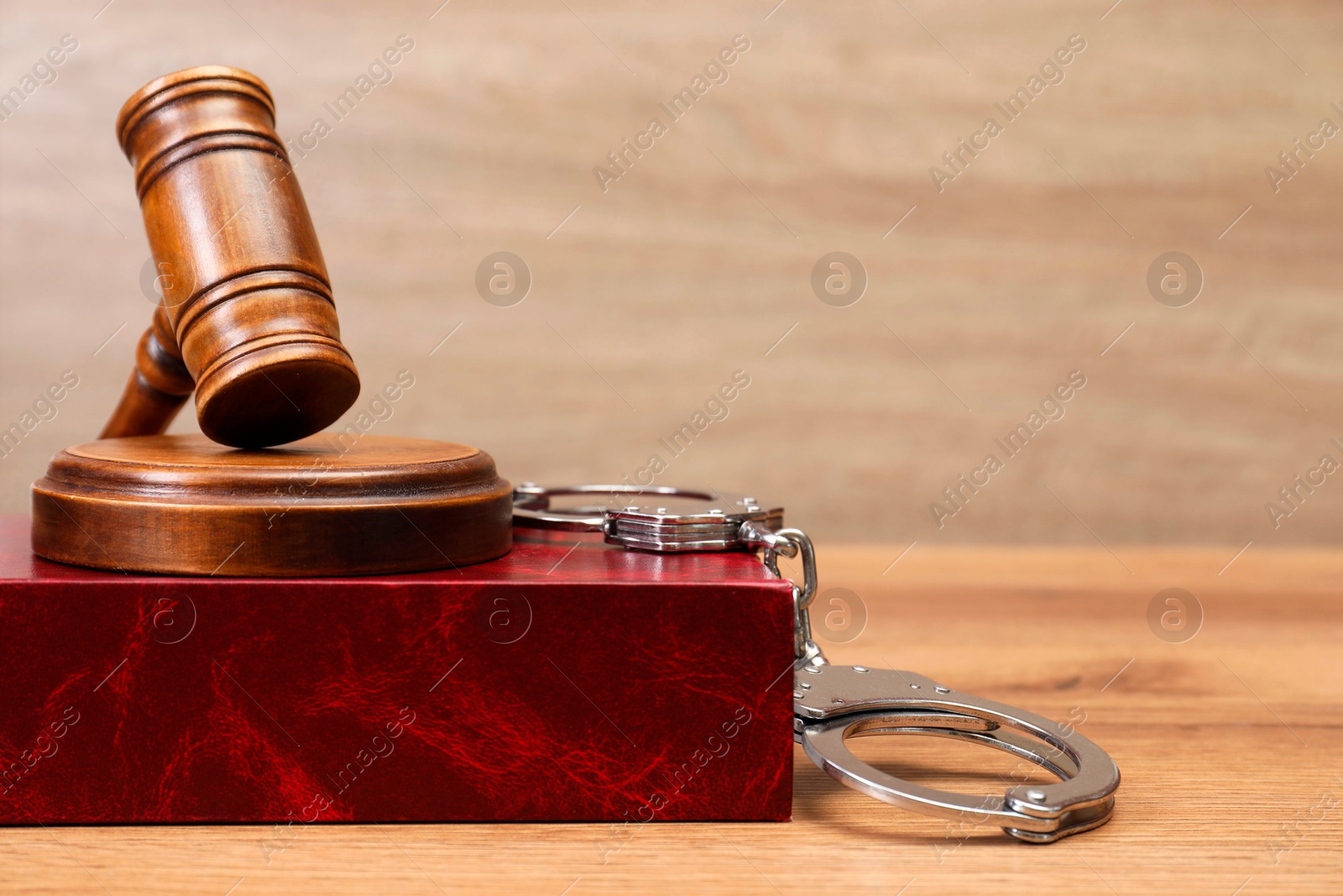 Photo of Book, judge's gavel and handcuffs on wooden table, space for text