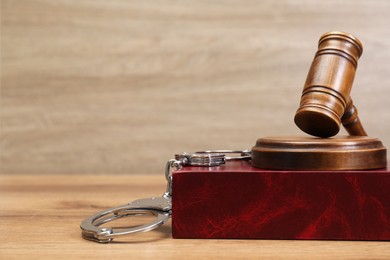 Photo of Book, judge's gavel and handcuffs on wooden table, space for text