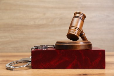 Book, judge's gavel and handcuffs on wooden table, space for text