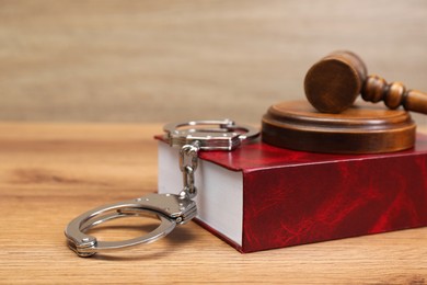 Book, judge's gavel and handcuffs on wooden table, space for text