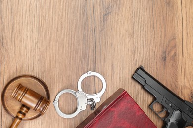 Book, judge's gavel, handcuffs and gun on wooden table, flat lay. Space for text