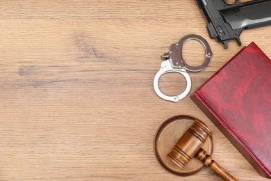 Book, judge's gavel, handcuffs and gun on wooden table, flat lay. Space for text