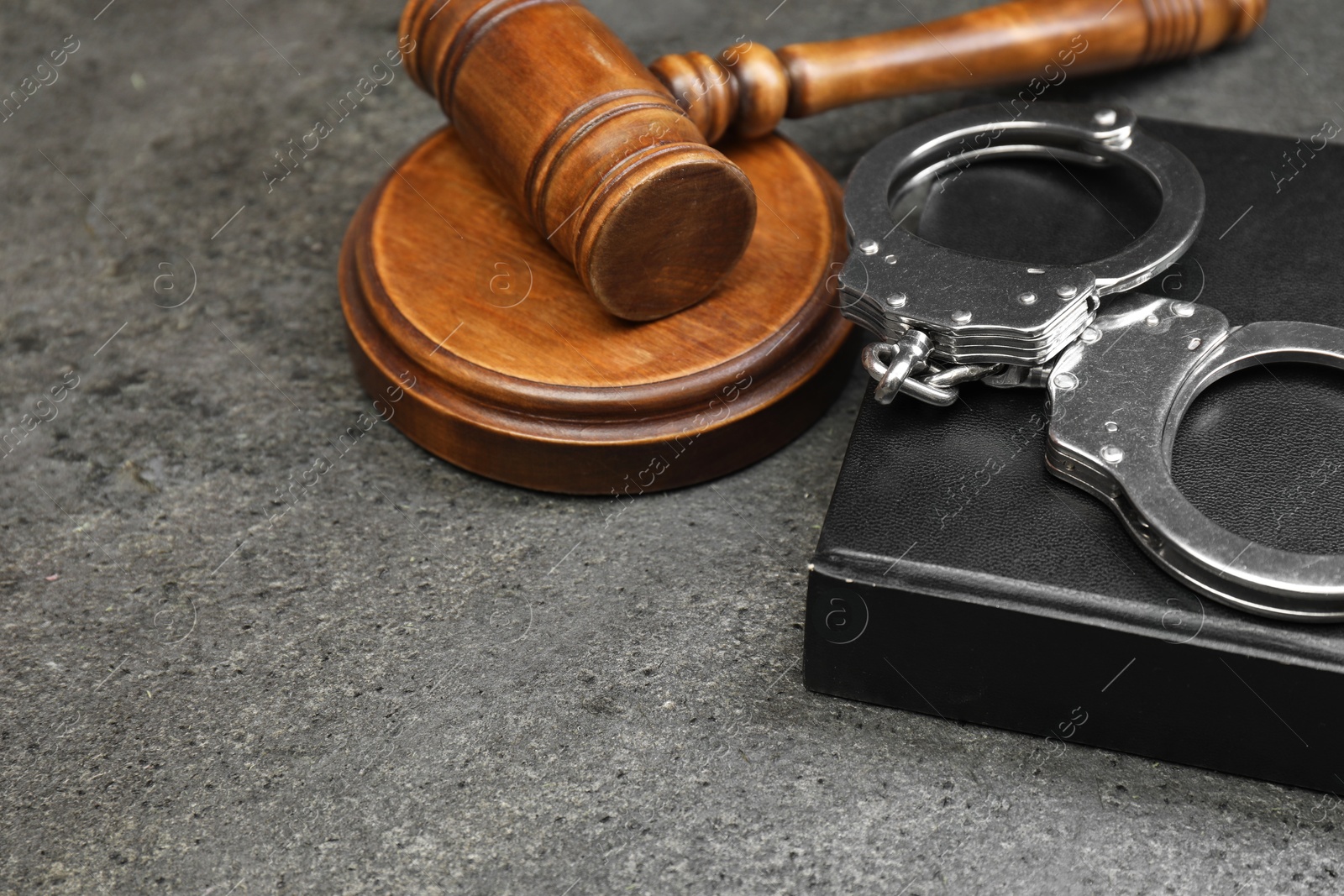 Photo of Book, judge's gavel and handcuffs on gray textured table, closeup. Space for text