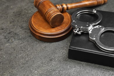 Book, judge's gavel and handcuffs on gray textured table, closeup. Space for text