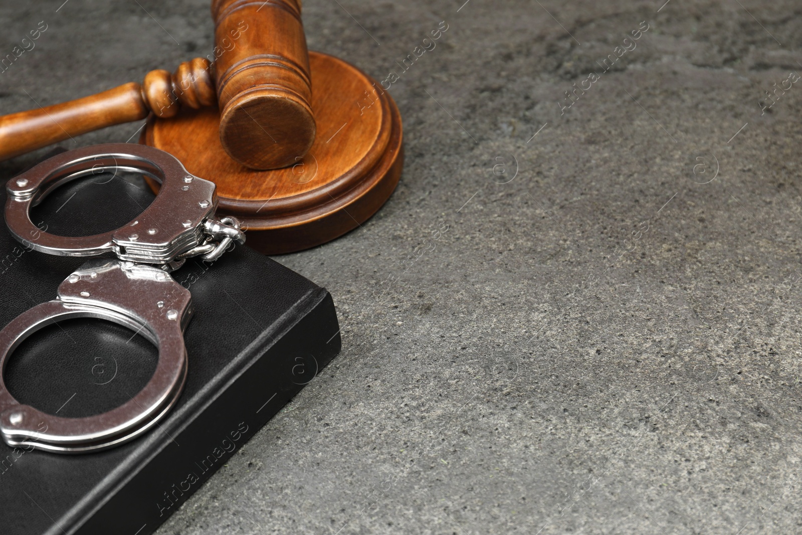 Photo of Book, judge's gavel and handcuffs on gray textured table, closeup. Space for text