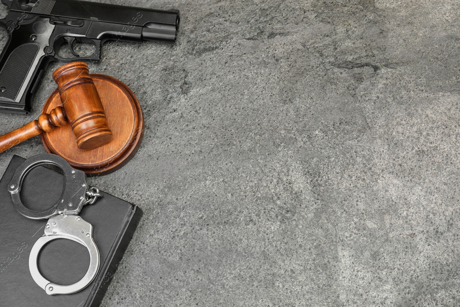 Photo of Book, judge's gavel, gun and handcuffs on gray textured table, flat lay. Space for text