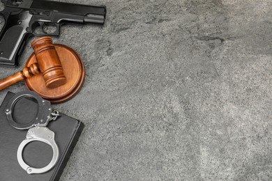 Book, judge's gavel, gun and handcuffs on gray textured table, flat lay. Space for text