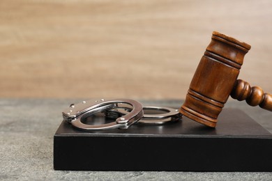 Book, judge's gavel and handcuffs on gray textured table, closeup. Space for text