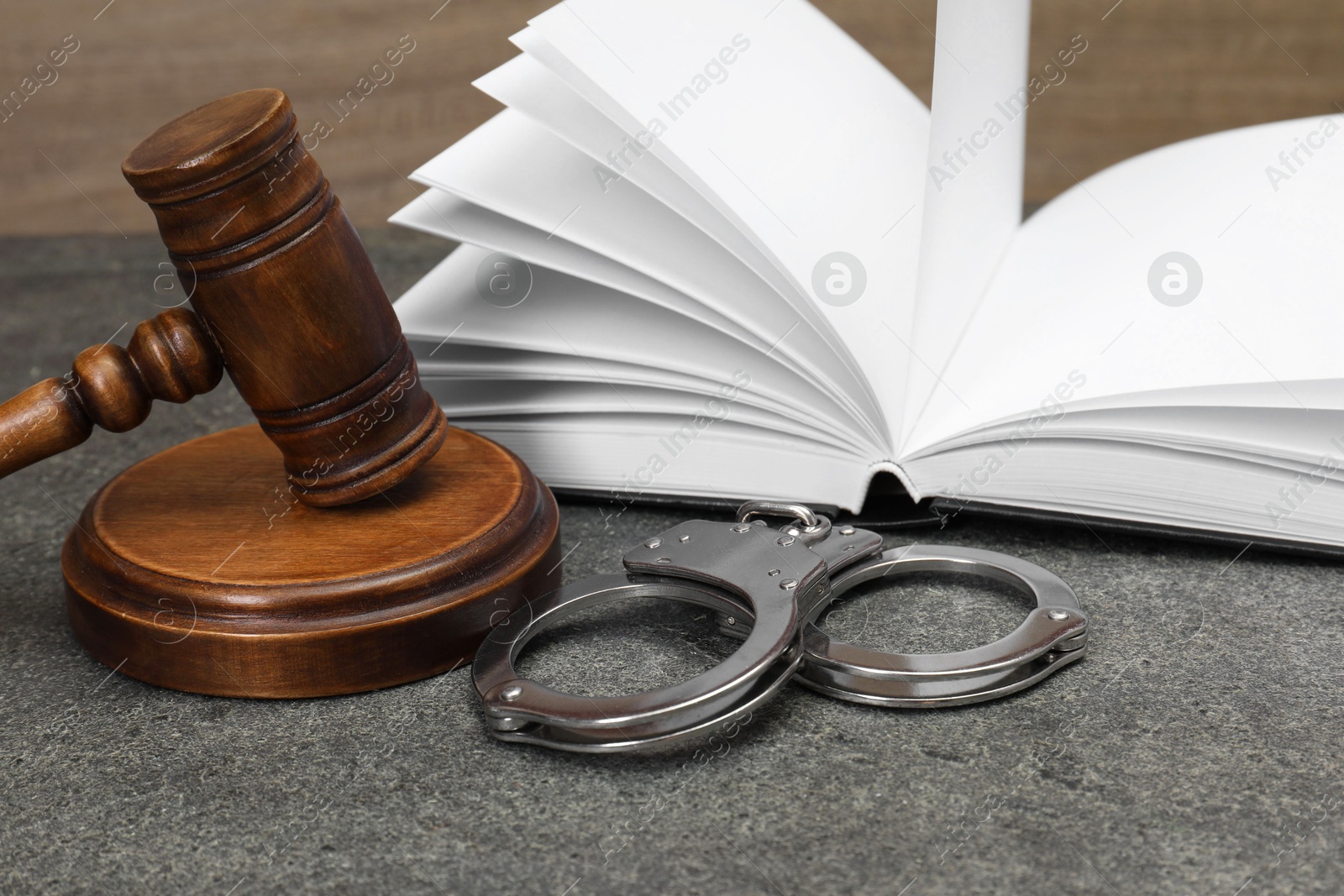 Photo of Book, judge's gavel and handcuffs on gray textured table, closeup