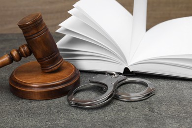 Book, judge's gavel and handcuffs on gray textured table, closeup