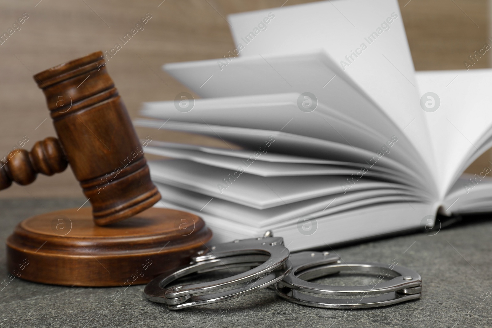 Photo of Book, judge's gavel and handcuffs on gray textured table, closeup