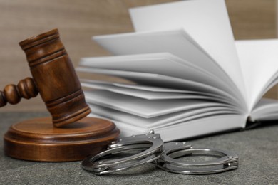 Photo of Book, judge's gavel and handcuffs on gray textured table, closeup