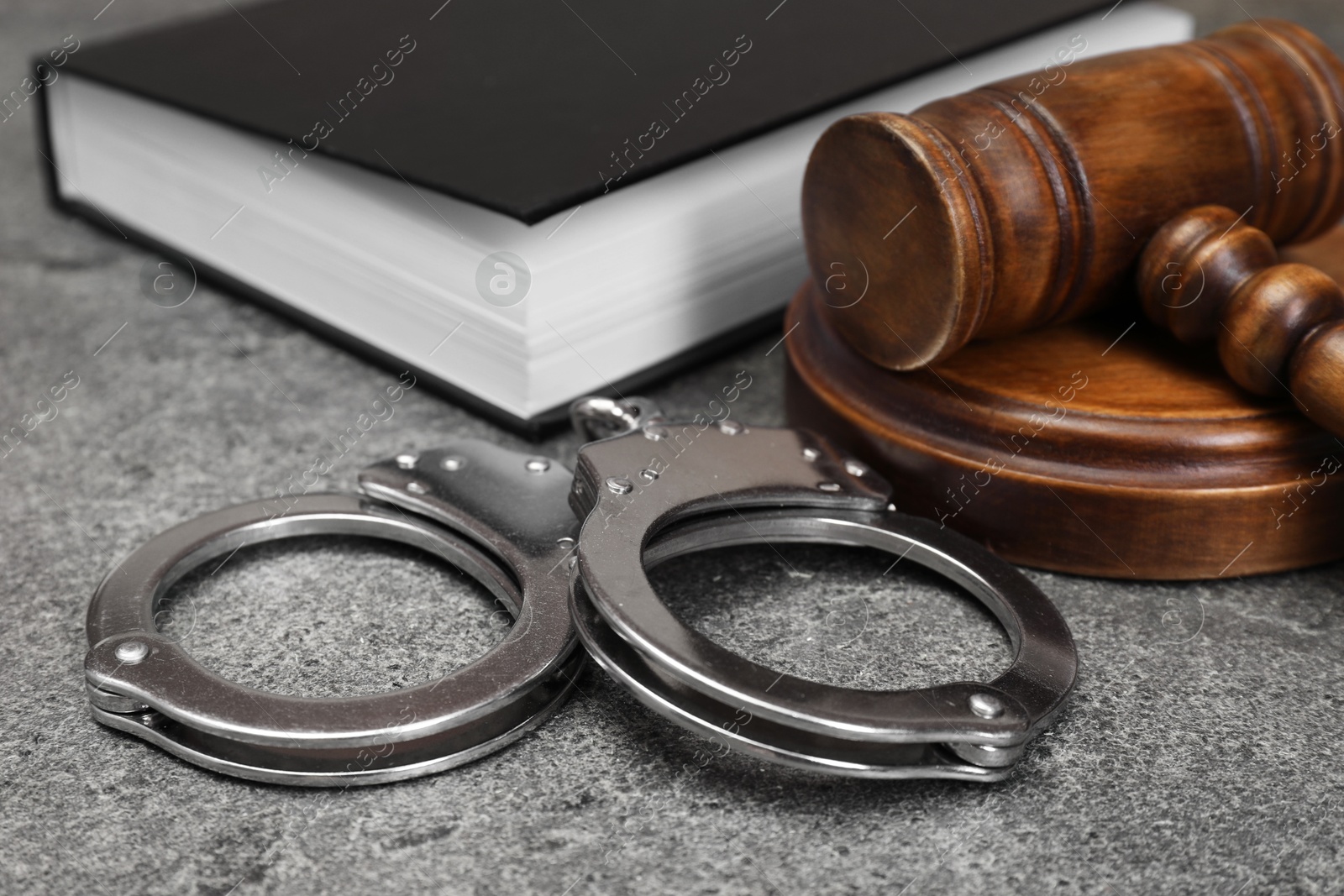 Photo of Book, judge's gavel and handcuffs on gray textured table, closeup