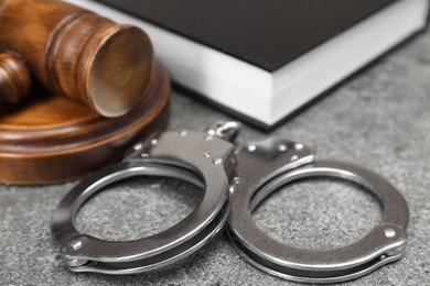 Photo of Book, judge's gavel and handcuffs on gray textured table, closeup