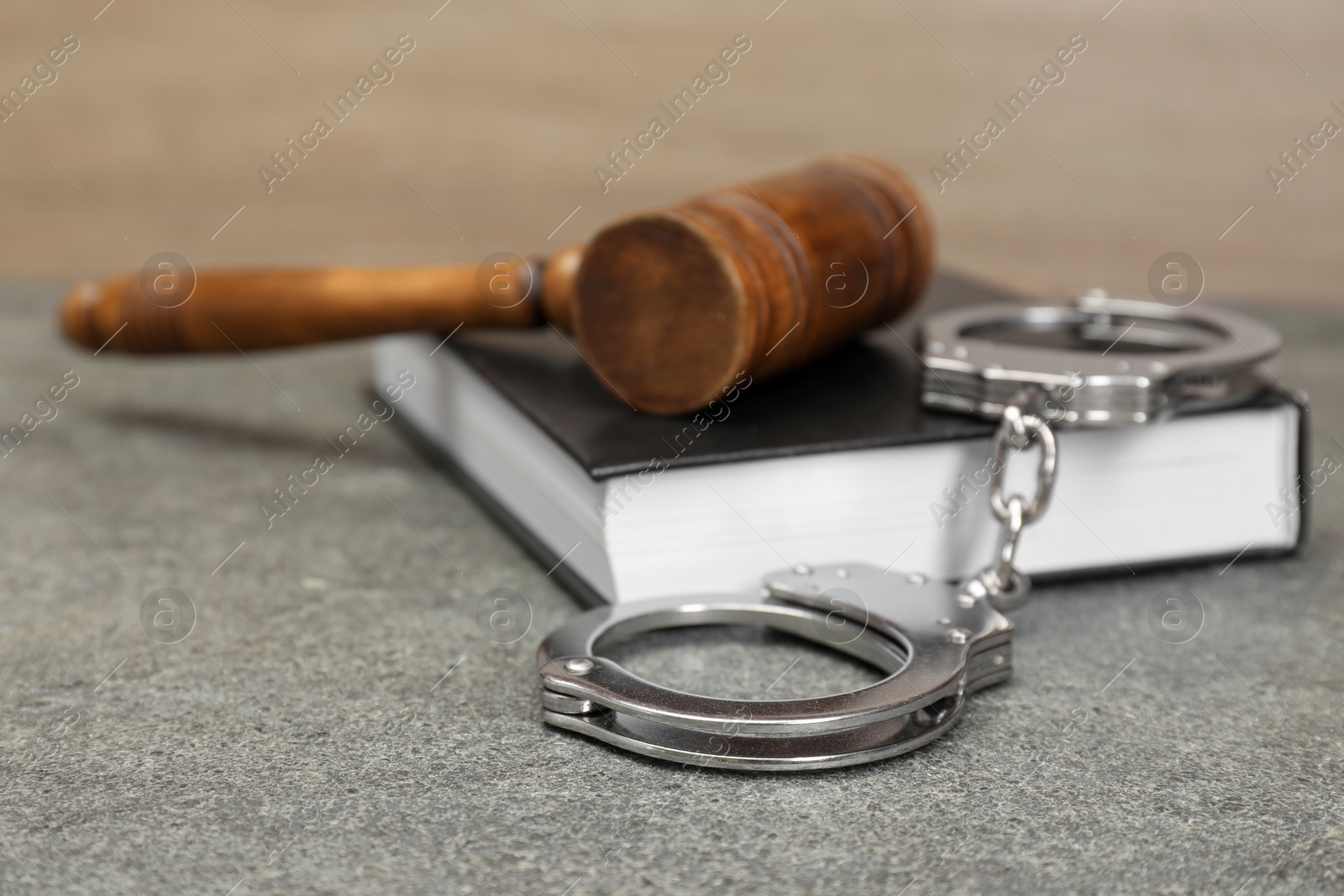 Photo of Book, judge's gavel and handcuffs on gray textured table, closeup