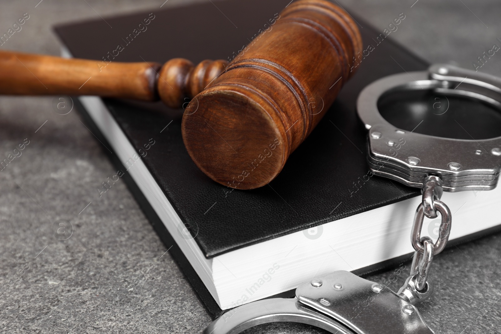 Photo of Book, judge's gavel and handcuffs on gray textured table, closeup