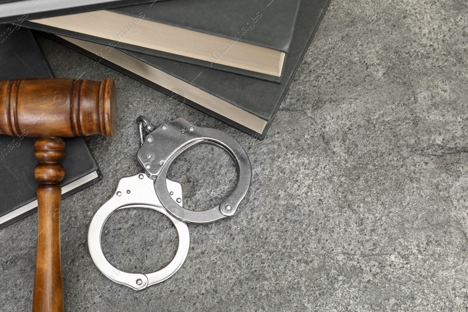 Photo of Books, judge's gavel and handcuffs on gray textured table, above view. Space for text