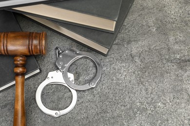 Books, judge's gavel and handcuffs on gray textured table, above view. Space for text