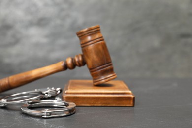 Photo of Judge's gavel and handcuffs on gray textured table, closeup. Space for text