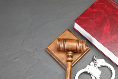 Book, judge's gavel and handcuffs on gray textured table, flat lay. Space for text