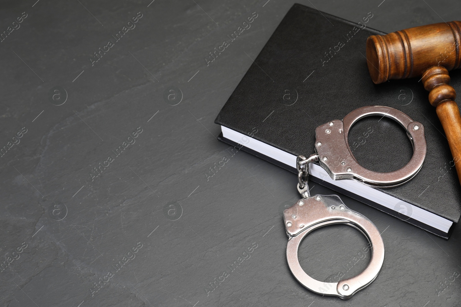 Photo of Book, judge's gavel and handcuffs on gray textured table, space for text