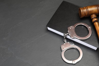 Book, judge's gavel and handcuffs on gray textured table, space for text