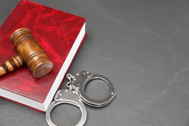 Book, judge's gavel and handcuffs on gray textured table, space for text