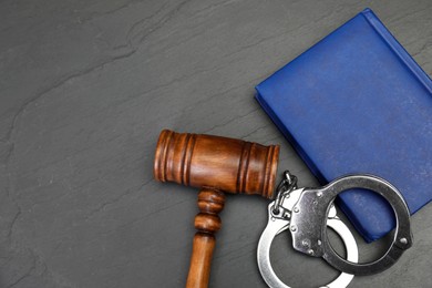 Book, judge's gavel and handcuffs on gray textured table, flat lay. Space for text