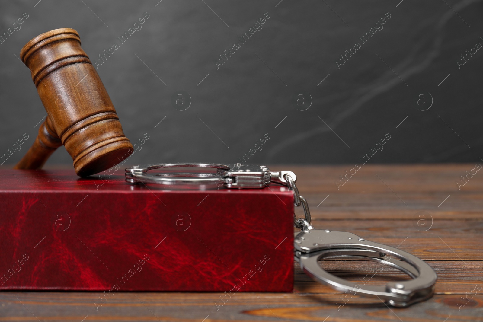 Photo of Book, judge's gavel and handcuffs on wooden table against gray background, space for text